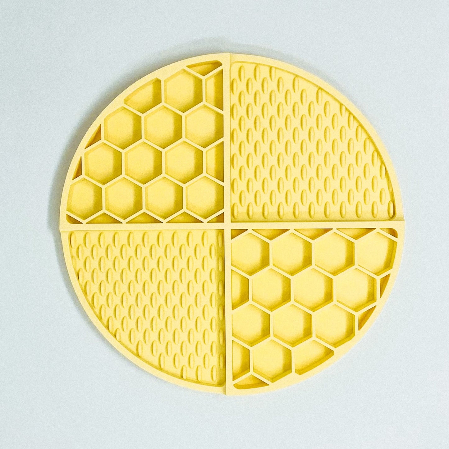 Light yellow silicone lick mat, separated into 4 sections. 2 sections are honeycomb shaped and 2 sections are licky texture.