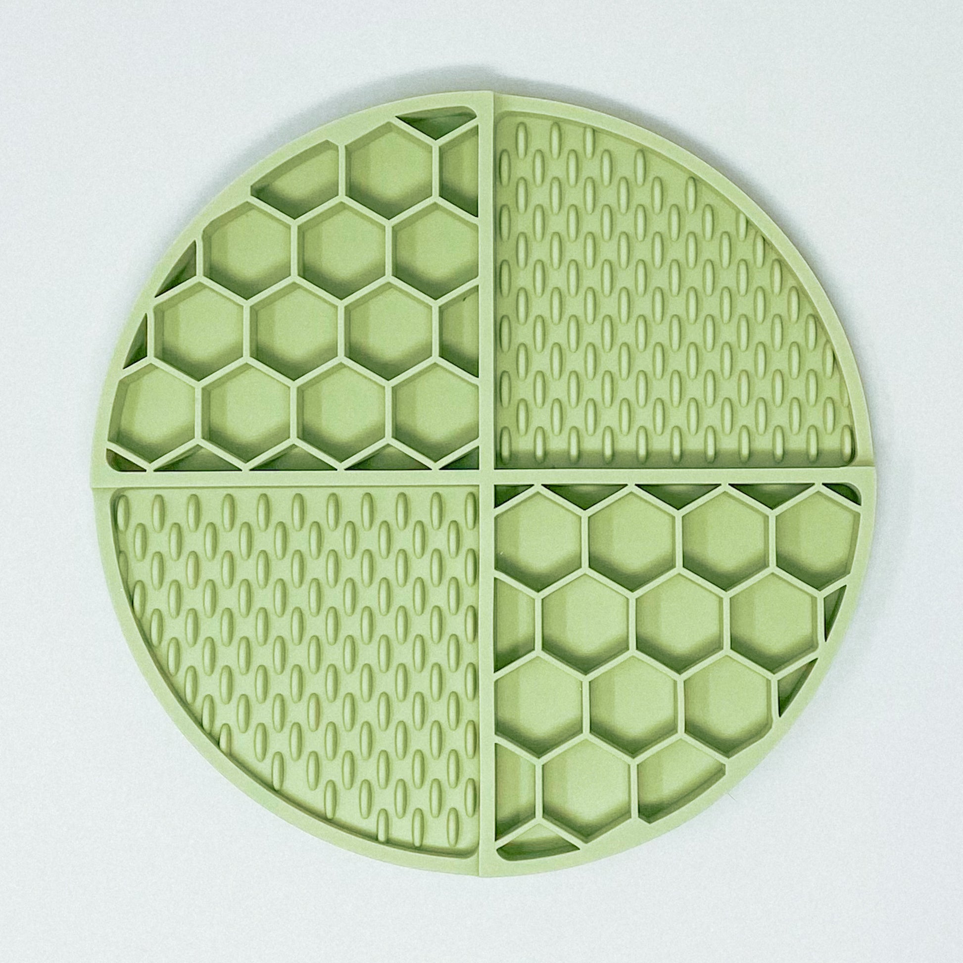 Sage green silicone lick mat, separated into 4 sections. 2 sections are honeycomb shaped and 2 sections are licky texture.